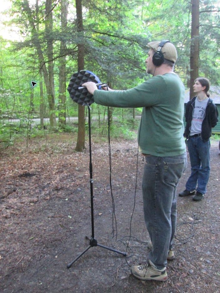 Matthew Boudreau recording outdoors in the woods with headphones and a parabolic microphone.